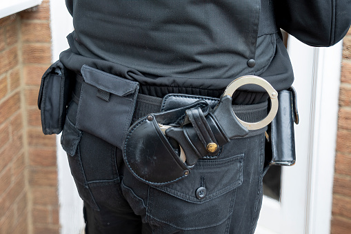 Close-up of a Police uniform jacket with utility belt and handcuffs prominent.