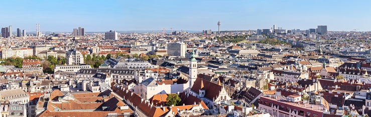 Wide angle panorama of Viennese red tiled roofs with modern high-rise buildings on horizon on clear sky summer day