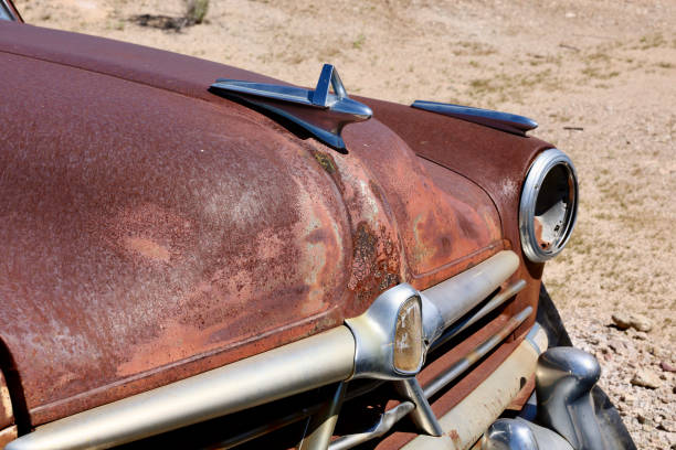 Detail view of the long metal fender and front portion of a vintage automobile in a junkyard.