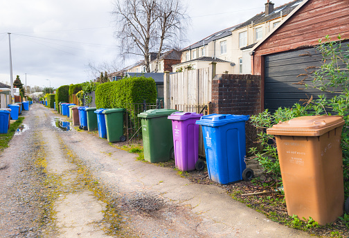 Glasgow, Scotland - A long lane behind houses with branded domestic wheelybins in colours denoting recycling, glass recycling, landfill and garden waste in Glasgow's West End.