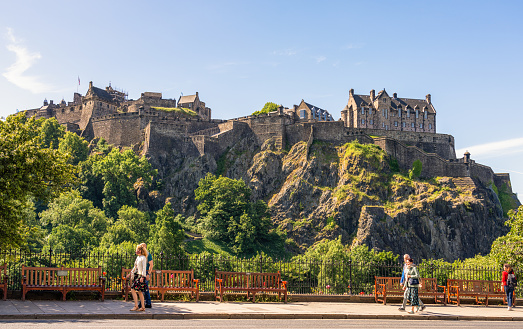 Edinburgh, Scotland - Pedestrians walking on Princes Street on a sunny day in July, with Edinburgh Castle in the background.