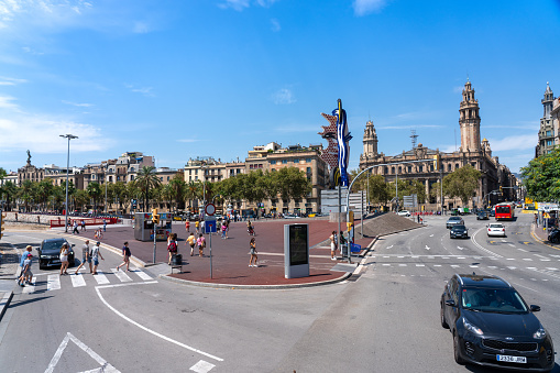 Pedestrians on a zebra crossing in a small square with the statue of The Face of Barcelona. Catalonia. Spain. August 15, 2023.