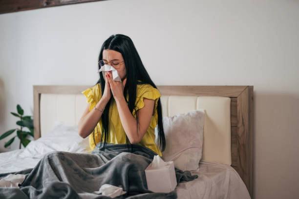 istock Sick woman blowing her nose, lying at home in bed covered with a blanket. 2149133996