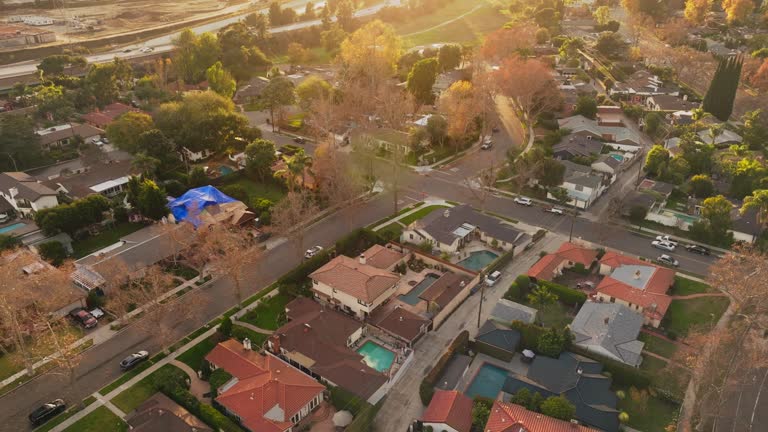 Aerial Footage of Upscale Neighborhood in California at Sunset, Establishing Shot of Large Homes with Pools and Pretty Yards Seen from Drone Above, Cars on Freeway in Background