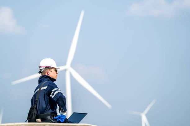 istock Focused engineer with a laptop conducts field analysis at a wind farm, wind turbines towering in the background. 2149136753