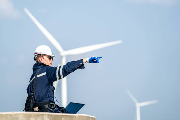 istock Focused engineer with a laptop conducts field analysis at a wind farm, wind turbines towering in the background. 2149136868
