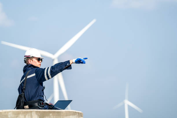 istock Focused engineer with a laptop conducts field analysis at a wind farm, wind turbines towering in the background. 2149136969