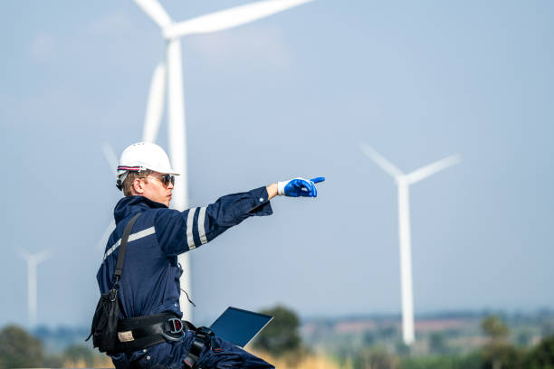 istock Focused engineer with a laptop conducts field analysis at a wind farm, wind turbines towering in the background. 2149137001