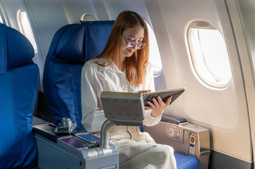 Happy young woman using her tablet while sitting alone on the plane by the window