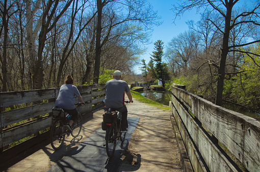 On a sunny Spring day, two cyclists cross a bridge and approach one of the locks on the Illinois Michigan Canal Towpath Trail, near Rockdale, Illinois.