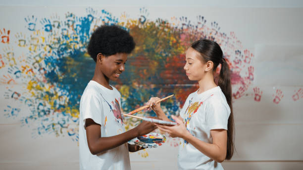 istock Smiling diverse children paint color on each other shirt at wall. Edification. 2149142995