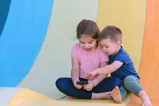 children sitting on the outdoor playground and looking at the phone. High quality photo