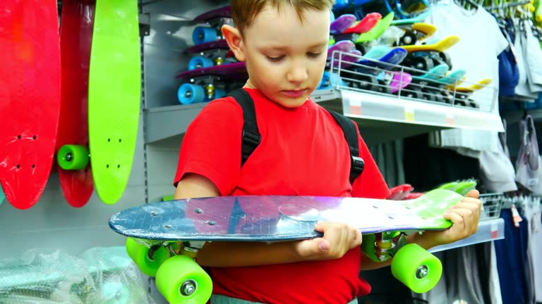 A cute boy looking at a skateboard in his hands in a skate shop
