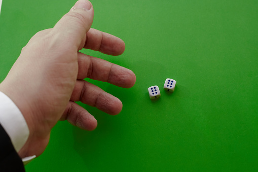 A manâs hand in a jacket throws two dice on a green cloth, two winning dice, the maximum number of points on two dice, dice in a casino, close-up.