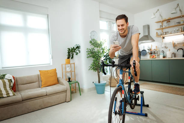 istock Young handsome man in sport clothes using smart phone while riding bike at home 2149147225