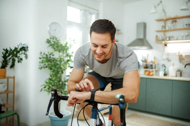 istock Young athletic man checking pulse on smart watch while riding bicycle in a domestic room at home 2149147239
