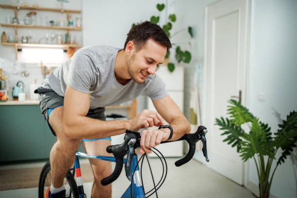 istock Young athletic man checking pulse on smart watch while riding bicycle in a domestic room at home 2149147241