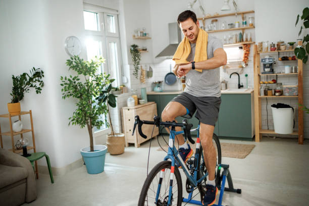istock Young athletic man checking pulse on smart watch while riding bicycle in a domestic room at home 2149147246