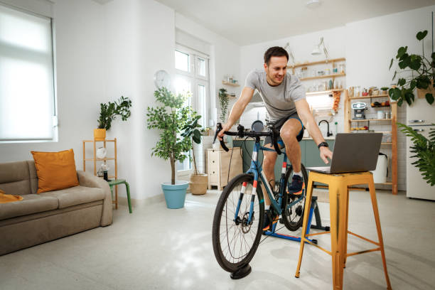 istock Young handsome man using laptop while exercising on a bike at home 2149147267