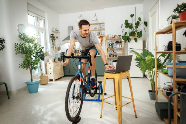 istock Young handsome man using laptop while exercising on a bike at home 2149147278