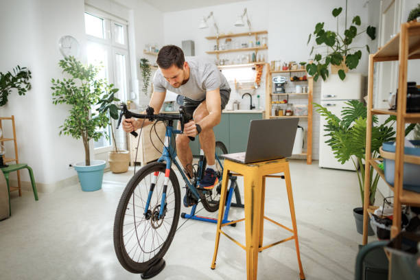 istock Young handsome man using laptop while exercising on a bike at home 2149147279