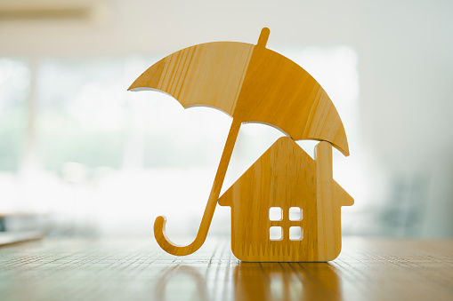 Wooden house model and real estate insurance ideas, individuals holding small umbrellas and sample homes. Housing insurance against impending loss and fire, building fire insurance concepts.