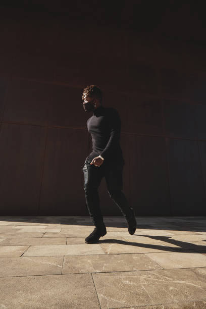 istock Stylish black man walking on pavement in dark clothes 2149148684