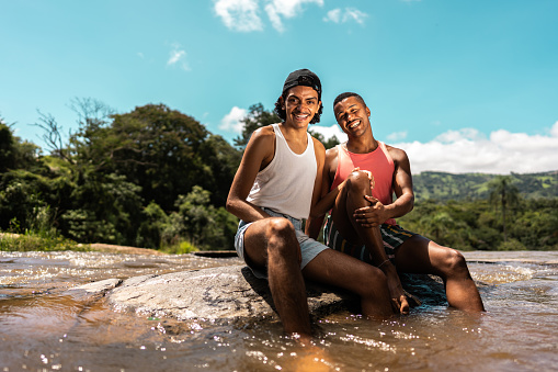 Portrait of a male friends sitting on ground on river at a mountain during eco tourism