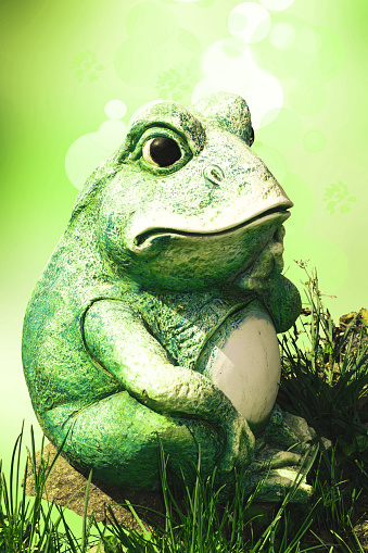Frog decoration background. A decorative old weathered ceramic frog figure sitting on a stone over abstract light green summer background.