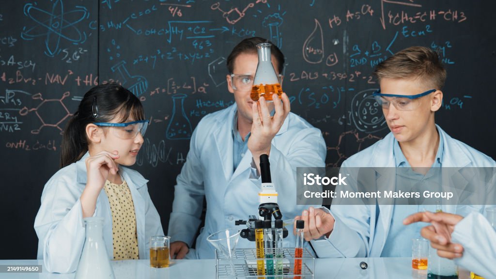 Edification Classes Teacher Holding Solution In Beaker While Student Doing Experiment ...