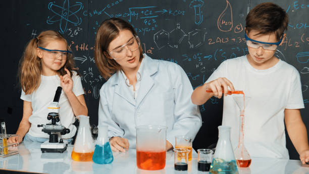 istock Caucasian boy mixing chemical liquid while teacher giving advice. Erudition. 2149150056