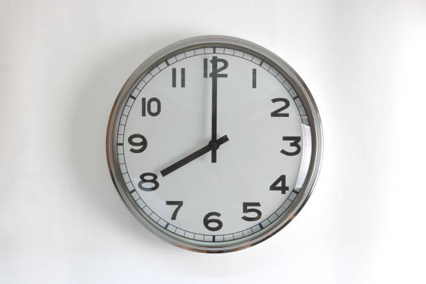 istock A round shape stainless steel wall clock with white face and hands set to 8 o'clock time. The clock is hanging on a wall. 2149151301