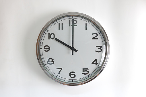 A round shape stainless steel wall clock with white face and hands set to 10 o'clock time. The clock is hanging on a wall.
