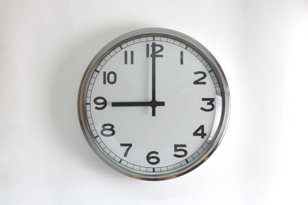 istock A round shape stainless steel wall clock with white face and hands set to 9 o'clock time. The clock is hanging on a wall. 2149151353