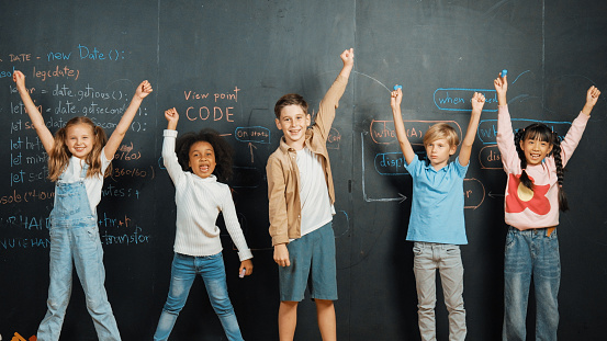 Diverse student raised hands up while standing at blackboard written with engineering prompt or coding, programing system code. Showing comment, asking questions, volunteering, voting. Erudition.