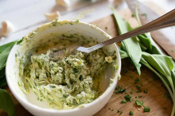 Fresh prepared herb butter on a wooden cutting board with ingredients. Delicious spread food background.