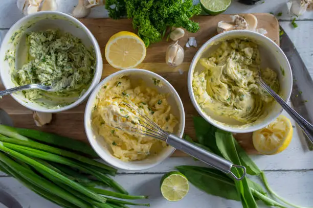 Herb butter, garlic butter and ramson butter in a bowl on a wooden cutting board with ingredients
