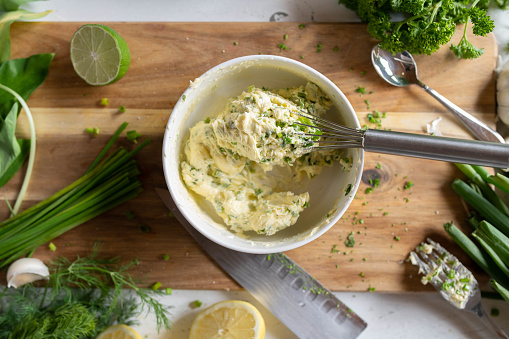 Fresh prepared herb butter on a wooden cutting board with ingredients. Delicious spread food background.