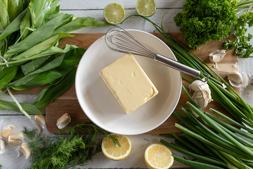 Ingredients for making herb butter on a cutting board. With ramson, parsley, garlic cloves, dill, lemon and butter