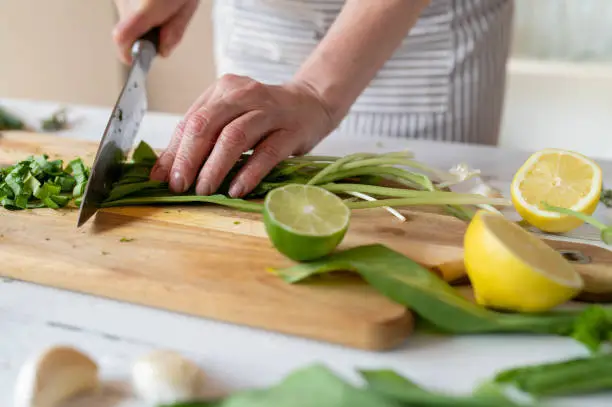 Cutting ramson or wild garlic leaves by woman´s hands in the kitchen on a cutting board