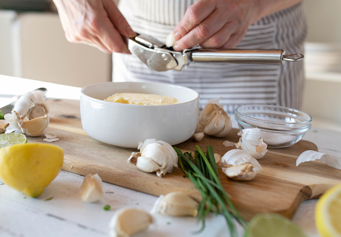 Woman putting a clove of garlic into a garlic press for making garlic butter in the kitchen.