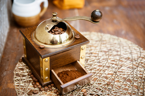 Roasted coffee beans and milled coffee in small wooden manual grinder with a brass handle. Copy space