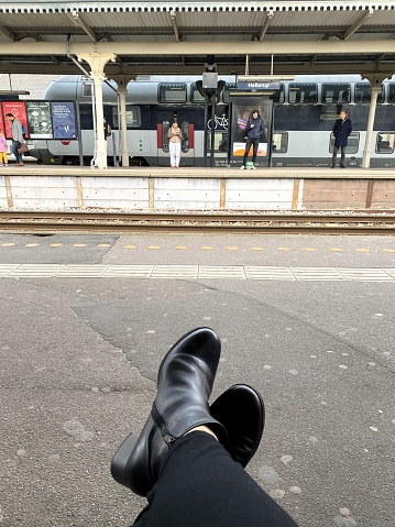 Feet up. A woman waiting for an S-train at Hellerup S-train station, Copenhagen, Denmark, on a rainy afternoon of April 18th.