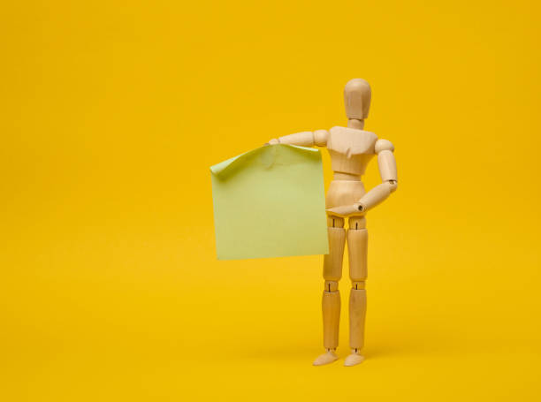 istock Wooden puppet puppet holding blank sticker sheet on yellow background 2149156200