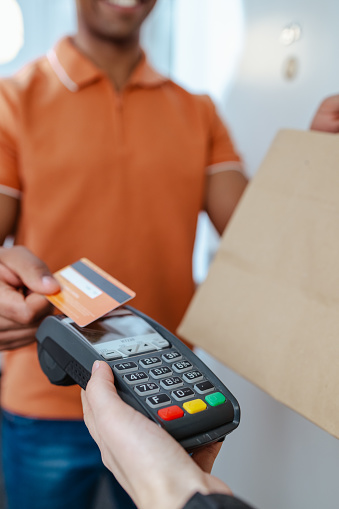 Close-up shot of a young African American man in an orange t-shirt paying with a credit card to the delivery person