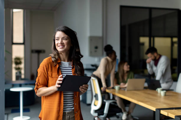 Beautiful smiled businesswoman standing inside modern office and looking at digital tablet