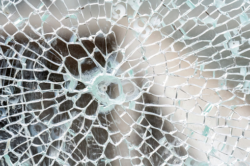 Closeup detail macro view of cracks spreading across a shattered glass panel, single point damage, broken tempered glass, building part, vehicle window, safety glass breaking abstract concept, nobody
