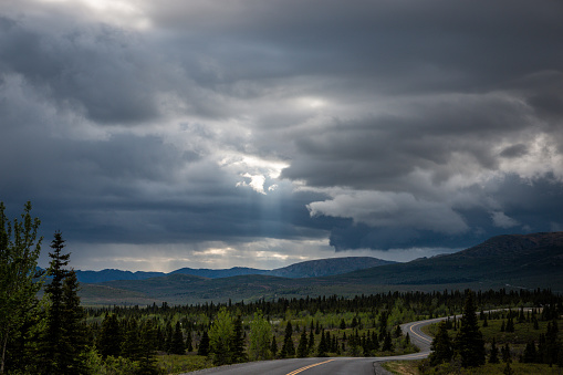 Winding road under moody sky with the sun rays streaming through and mountains in the background