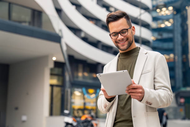 Young happy businessman using digital tablet outside of modern work place