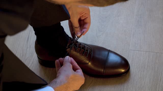 A man in a suit ties his shoelace on his luxurious black shoes